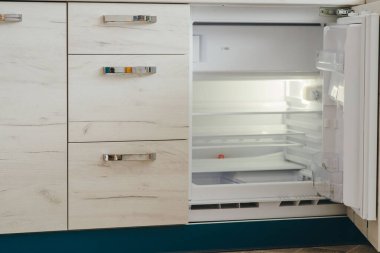 A picture of an open empty built-in fridge and a kitchen drawers on the left. Kitchen close up. clipart