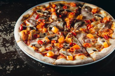 Eritilmiş peynirli İtalyan pizzası, domates, kırmızı biber, mantar ve kahverengi bir masada otlar. Lezzetli sıcak pizza..