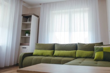 Ahşap döşemeli, yeşil kanepeli ve beyaz kitaplıklı modern bir oturma odası..