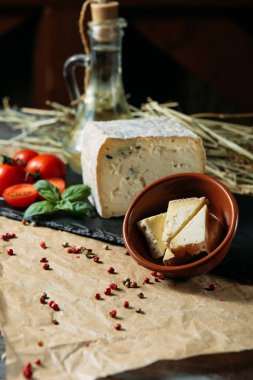 Baharatlı, domates, kiraz ve fesleğenli ev yapımı beyaz peynir. Koyu ahşap kesim tahtasının üzerinde doğranmış peynirli küçük bir kase..