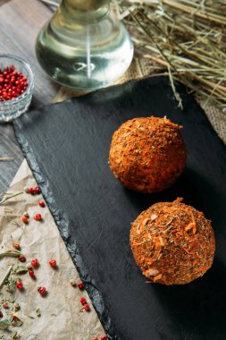 Yağda iki mozzarella topunun yakın planda siyah ahşap bir tahtanın üzerinde farklı baharatlar var..