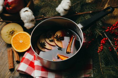 Narenciye, elma ve baharatlı sıcak şarap. Alüminyum kapta, masa örtüsünün üzerinde. Kürk ağacı dalları, kırmızı böğürtlen ve pamuklu kış tatili havası.