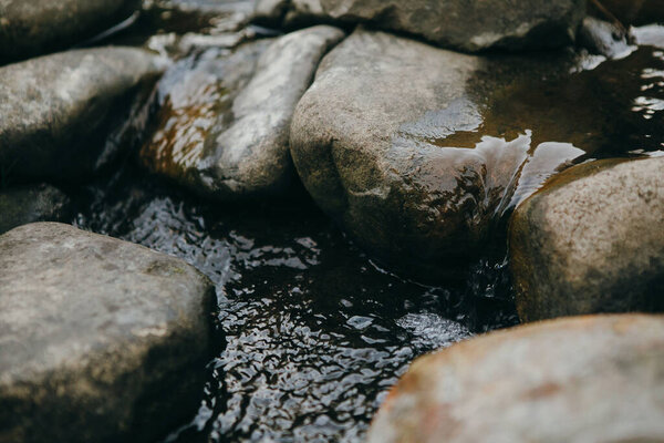 Rocky detail of flowing river. Water flows between smooth round stones in mountain river.