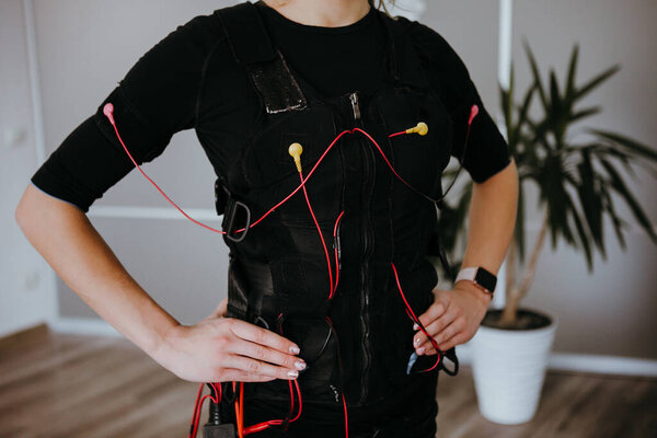 Woman in EMS electro stimulation suit with cables.