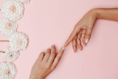 Kadının elleri birbirine dokunuyor, solda beyaz yıldız çiçekleri, pembe arka planda. Bağlantı ve anlayış kavramı.
