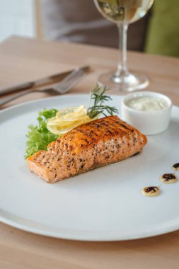 Güzel servis edilmiş somon balığı bifteği ve bir bardak beyaz şarap. Limon, salata ve biberiyeli ızgara somon bifteği..
