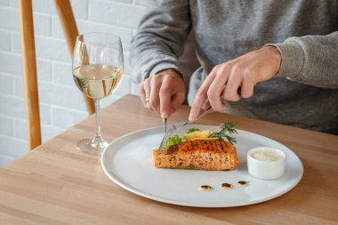 Somon balığı bifteği yiyen adamın yatay yakın çekimi. Limonlu, salatalı ve biberiyeli ızgara somon bifteği, beyaz şarap ve beyaz sos..