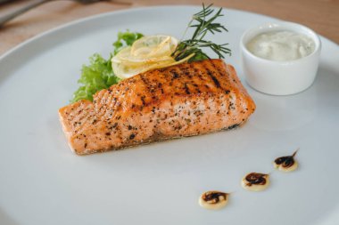 Somon balığı bifteği ve beyaz sos yakın çekim. Limon, salata ve biberiyeli ızgara somon bifteği..