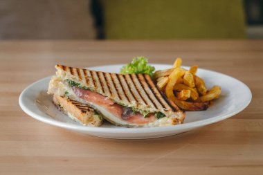 Somon kulübü sandviçleri beyaz ekmek üzerinde, patates kızartması ve salata bir restoranda, ahşap bir masada..