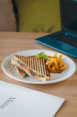 Somon kulübü sandviçleri beyaz ekmek üzerinde, patates kızartması ve salata bir restoranda, ahşap bir masada..