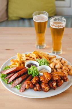 Büyük sıcak bira tabağı sosis, patates kızartması, tavuk ve sosis ve arka planda iki bardak bira..