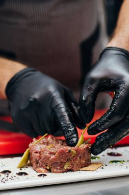 Etli tart pişirme işlemi. Adamın elleri doğranmış bifteğe kapari ekliyor.