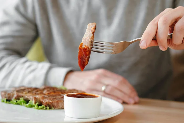 男の手は赤いトマトソースで焼きステーキの一片を浸し — ストック写真