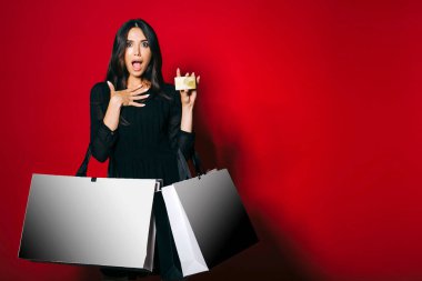 Koyu kırmızı arka planda elinde altın bir kredi kartı taşıyan büyüleyici bir kadın..