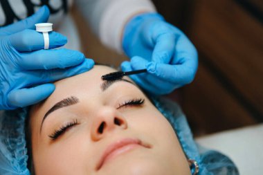 Güzellik salonunda kadın müşterisinin kaşlarını şekillendiren ve boyayan bir sanatçı. İşlem devam ediyor.