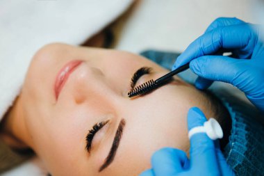 Güzellik salonunda kadın müşterisinin kaşlarını şekillendiren ve boyayan bir sanatçı. İşlem devam ediyor.