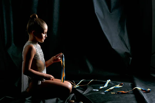 Piękna Dziewczyna Nastolatka Gimnastyczka Białej Sukience Sportowej Patrząc Jej Medale — Zdjęcie stockowe