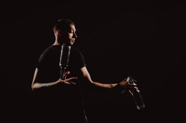 Portre iş başında. Genç ve yakışıklı barmen kokteyl yapıyor. Barmenlerin performansı titretici ve şişe ile siyah üzerine izole edilmiş.