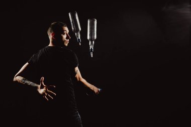 Portre iş başında. Genç ve yakışıklı barmen kokteyl yapıyor. Barmenlerin performansı titretici ve şişe ile siyah üzerine izole edilmiş.