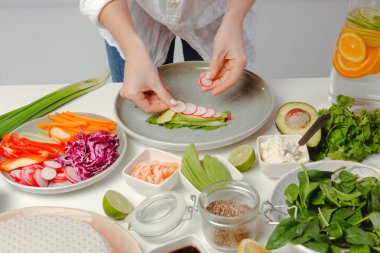 Kadınların elleri börek hazırlıyor, dilimlenmiş turp, fesleğen, salatalık ve tohumları mutfak masasına koyuyor..