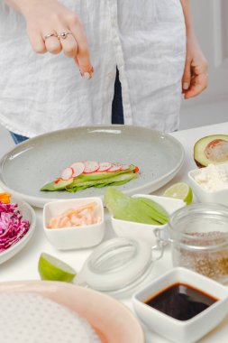 Yumurta rulolarını turp, fesleğen, salatalık ve çekirdekle hazırlayan kadının dikey fotoğrafı..