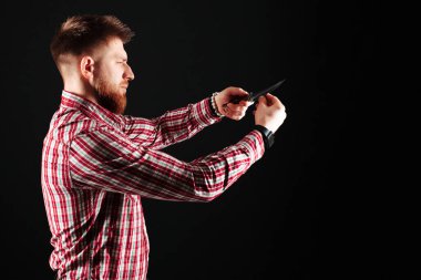 Siyah arka plandaki keskinliği test etmek için elinde bıçak tutan, kareli tişörtlü genç bir adam. Şef aşçı aletlerini test ediyor..