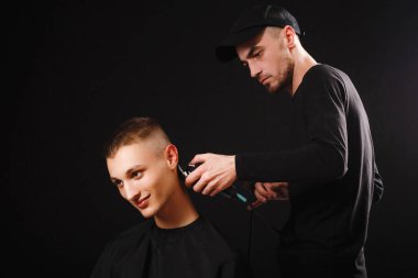 Siyah arka planda berber dükkanında profesyonel elektrikli makasla kırpılan genç adamın portresi.