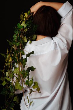 Güzel esmer, genç bir kadın elinde yeşil bir dalla arkasında koyu bir arka plan bırakıyor..