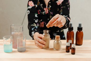 Kızın eli pipeti tutuyor, masanın üzerinde çeşitli kozmetik yağlar var. Yaşlanma karşıtı tedaviler için modaya uygun kozmetik ürünler. El yapımı organik cilt bakımı.
