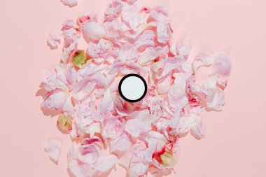 Pembe çiçek yapraklarının arka planında vücut ve yüz kremi kavanozu. El yapımı organik güzellik ürünü.