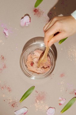 Çiçek yaprakları ve yapraklarla çevrili, sade masada killeri karıştıran bir kadın görüntüsü..