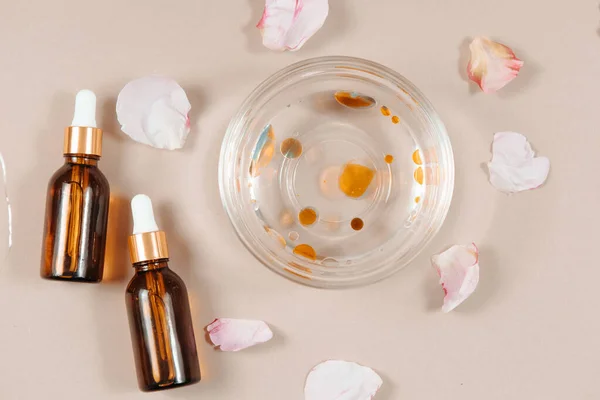 Organic beauty face oil serum bottles for cosmetic treatment skin care, bowl of water with oil and flower petals on soft pastel background.