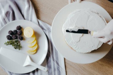 Karantina sırasında üzerinde meyve, böğürtlen, limon ve nane olan limonlu kek pişiren bir ev hanımı manzarası. Ev yapımı limonlu kek tarifi. Evde yemek pişirmek..