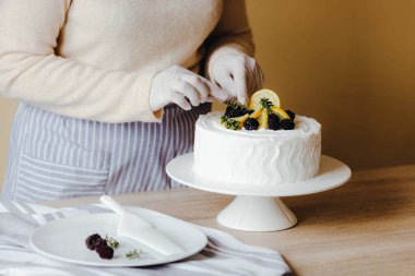Mutfaktaki ev hanımı karantina sırasında limonlu pastayı meyve, böğürtlen, limon ve nane ile süslüyor. Organik ev yapımı limonlu kek tarifi.