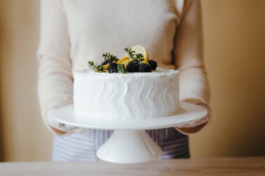 Mutfakta elinde meyveli limonlu pasta, böğürtlen, limon ve karantina sırasında naneli şeker tutan bir ev kadını. Ev yapımı limonlu kek tarifi. Evde yemek pişirme kavramı.