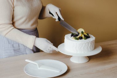Genç bir ev kadınının elleri limonlu keki parçalara ayırdı. Limonlu, böğürtlenli, naneli ve kremalı kutlama pastası. Organik limonlu kek tarifi..