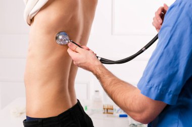 Ciğerlerde pnömoni, koronavirüs ve kovid19 enfeksiyon aranıyor. Steteskoplu bir erkek doktor genç çocuğun akciğer ve kalp atışlarını dinliyor. Sağlık hizmetleri. Aile doktoru.