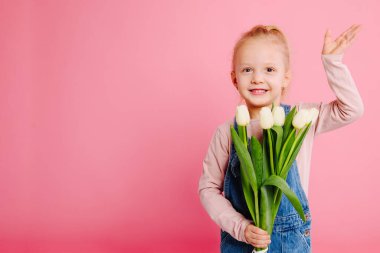 Genç, sevimli, gülümseyen kız pembe arka planda beyaz laleler tutuyor. Mutlu çocukluk kavramı. Anneler günün kutlu olsun ya da çocuklar günün kutlu olsun.