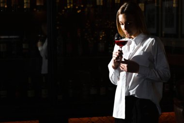 Sarışın, genç, güzel kız şarap garsonu elinde bir bardak kırmızı şarap tutuyor ve kokluyor. Şarap aromasını takdir eder..