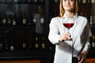 Sarışın, gülümseyen kız şarap garsonunun elinde bir kadeh kırmızı şarap tutarken yakın plan fotoğrafı. Şarap buketi kokan şarap garsonu..