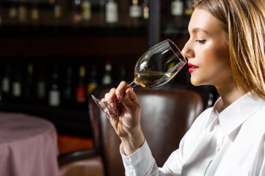 Sommelier genç sarışın kız bir bardak kırmızı kuru şarap içiyor ve tadıyor..