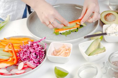 Yumurtalı börek yapma süreci. Sağlıklı yemek hazırlığı. Kadının elleri dilimlenmiş sebzeleri pirinç kağıdına koyuyor..