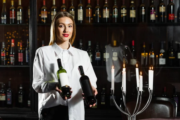 Young pretty girl sommelier serving & presenting bottles of red and white of wine. Appreciates the aroma of wine.