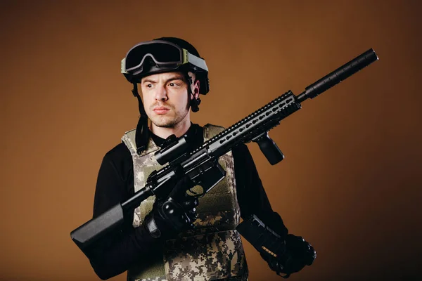 Soldier with gun inserts magazine with cartridges on brown background. Concept of war. Veterans, comrades, soldiers. Man in uniform.