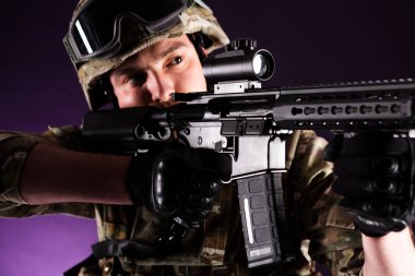 Silahlı asker menekşe arkaplanından bakıyor. Savaş kavramı. Gaziler, yoldaşlar, askerler. Üniformalı adam.