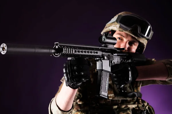 Soldier with gun is looking through the scope on violet background. Concept of war. Veterans, comrades, soldiers. Man in uniform.