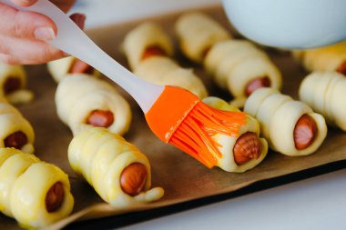 Ev hanımı hamurun içinde sosis pişiriyor. Yumurta sarısını fırçala. Karantina evi resepsiyonları.