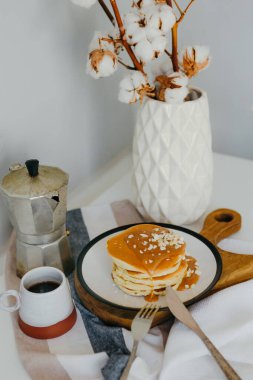 Mutfaktaki beyaz masada kahve makinesinin yanında tuzlu karamel ve fıstıklı gözleme. Karantinada sabah kahvaltısı. Ev yapımı lezzetli krep tarifi..