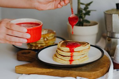 Mutfaktaki beyaz masada kahve makinesinin yanına ahududu sosu döken bir kız. Karantinada sabah kahvaltısı. Ev yapımı lezzetli krep tarifi..