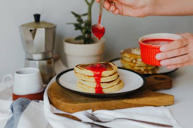Mutfaktaki beyaz masada kahve makinesinin yanına ahududu sosu döken bir kız. Karantinada sabah kahvaltısı. Ev yapımı lezzetli krep tarifi..